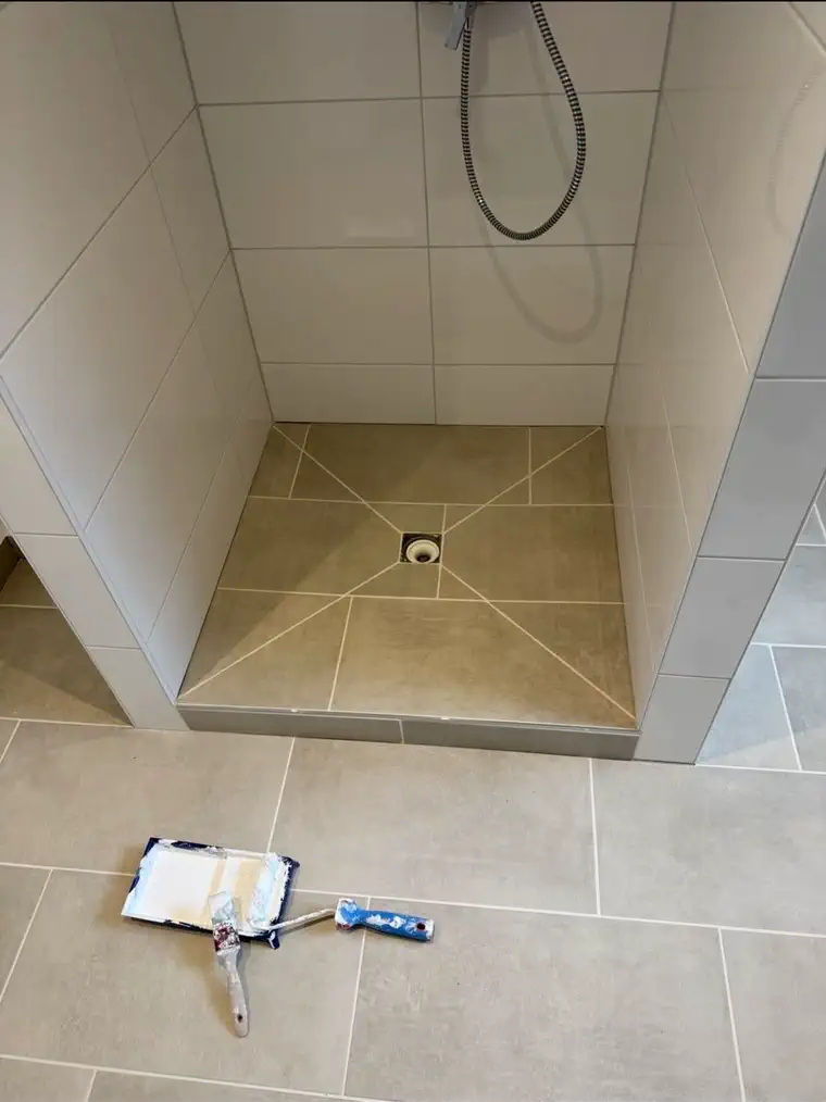 Fertige Dusche mit weissen Wandplatten und dem Bodengefälle sternförmig zum Ablauf