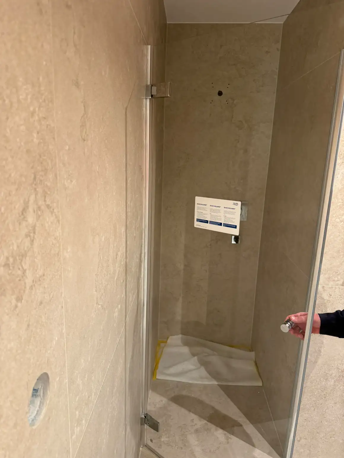 Bodenebene Dusche mit rahmenloser Glastür und grossformatigen Platten in heller Travertin-Optik