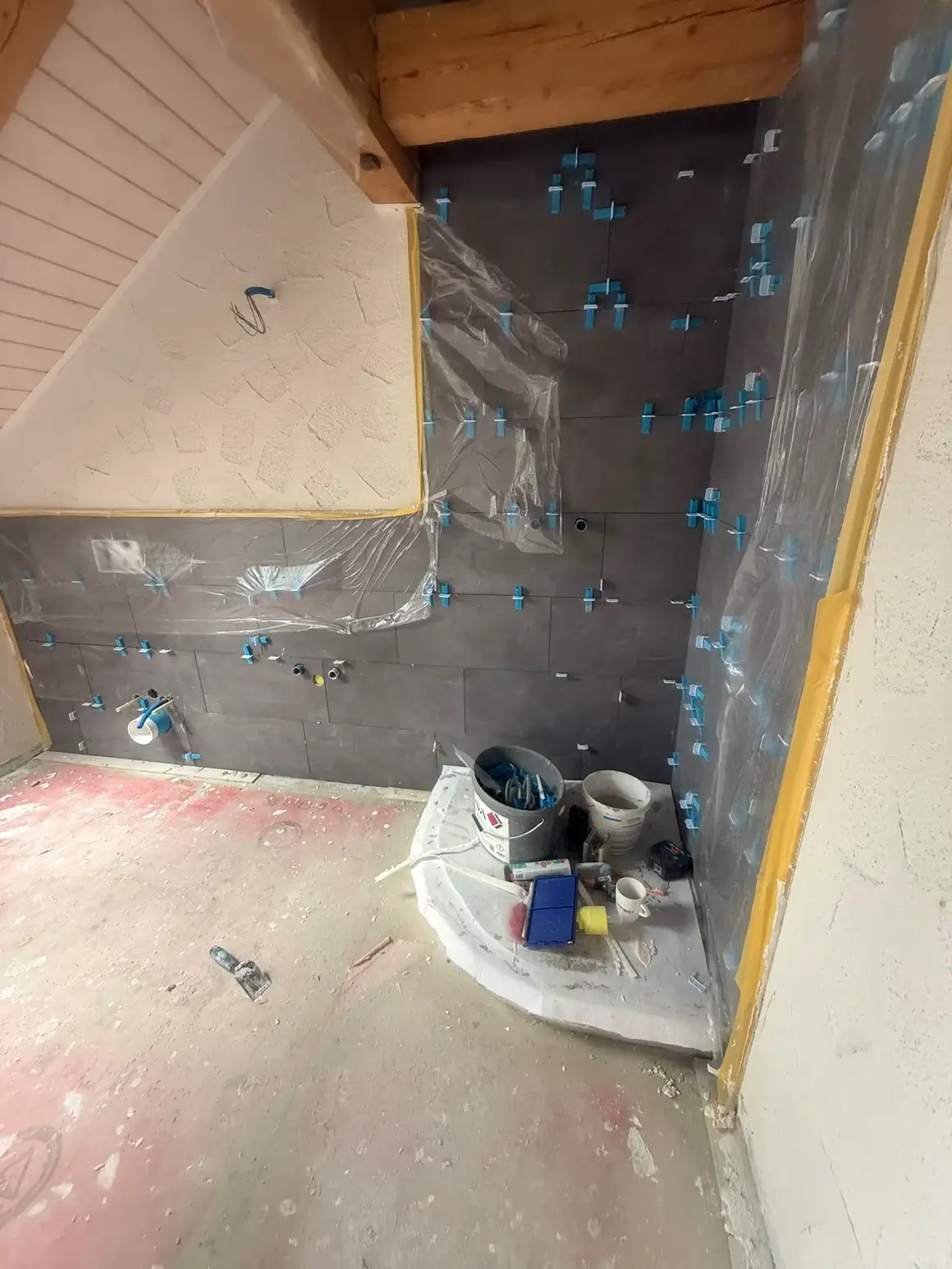 Anthrazitfarbene Wandplatten im Rohbau, mit Nivellierkeilen gesetzt und bis an die Dachschräge gearbeitet