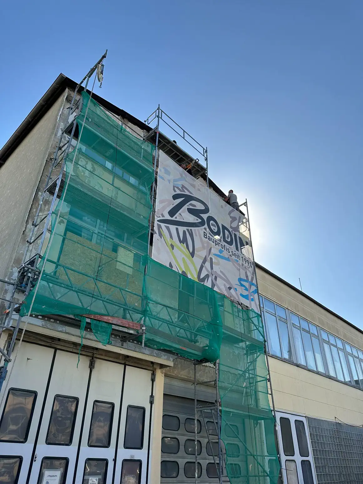 Eingerüstetes Gewerbegebäude mit Schutznetz über die ganze Giebelseite