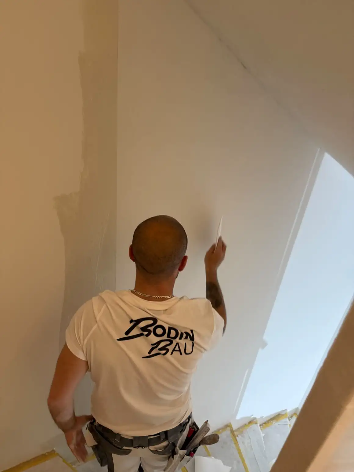 Maler von Bodin Bau beim Glätten der Wandfläche im Treppenhaus